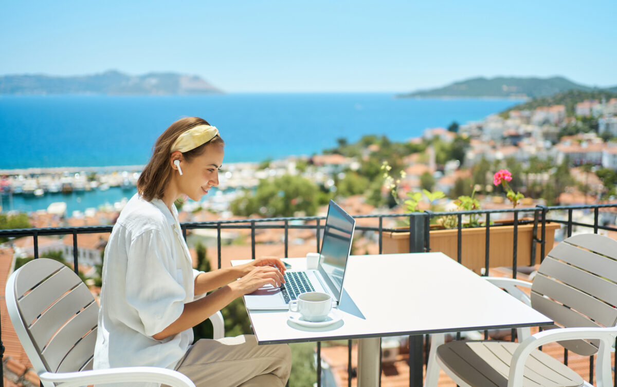 Digital nomad typing on a laptop at a seaside café, illustrating the freedom of remote internships and location-independent work.