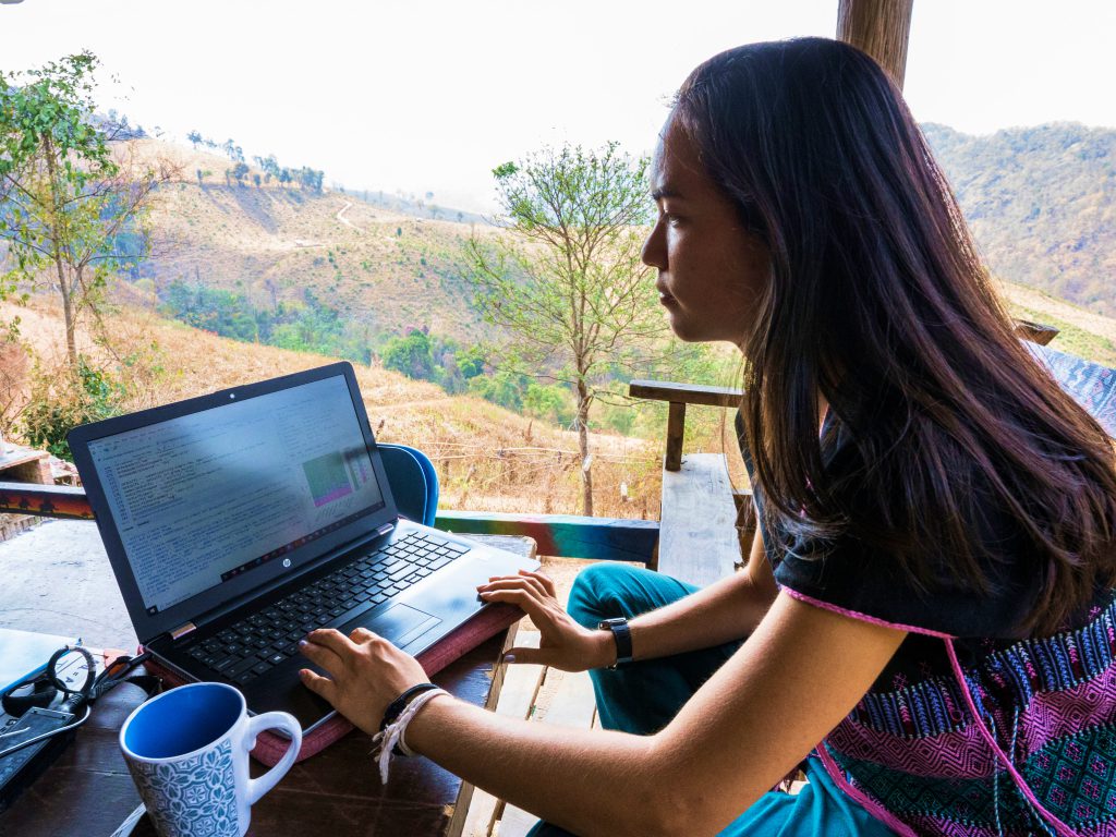 Female digital nomad working on a laptop in a scenic mountain environment, highlighting remote internship flexibility and online TEFL teaching.