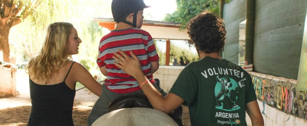 Volunteers assisting a young rider during an equine therapy session, reflecting specialized internships in Argentina.